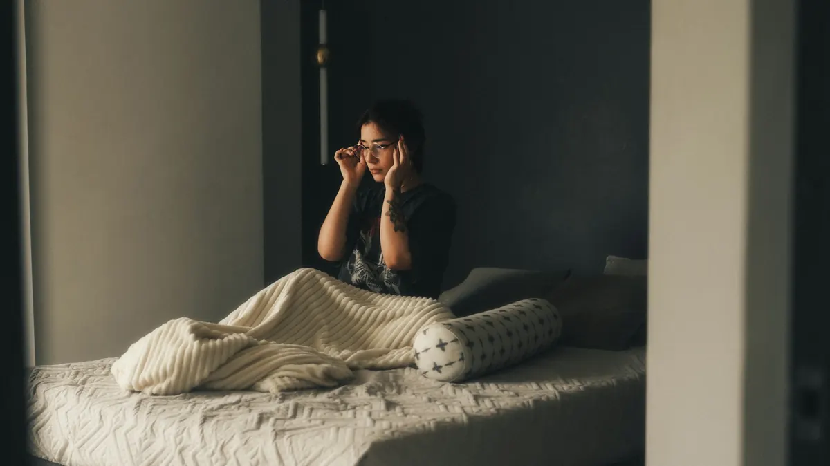 Personne assise dans son lit la nuit, les mains sur les tempes, l'air inquiet