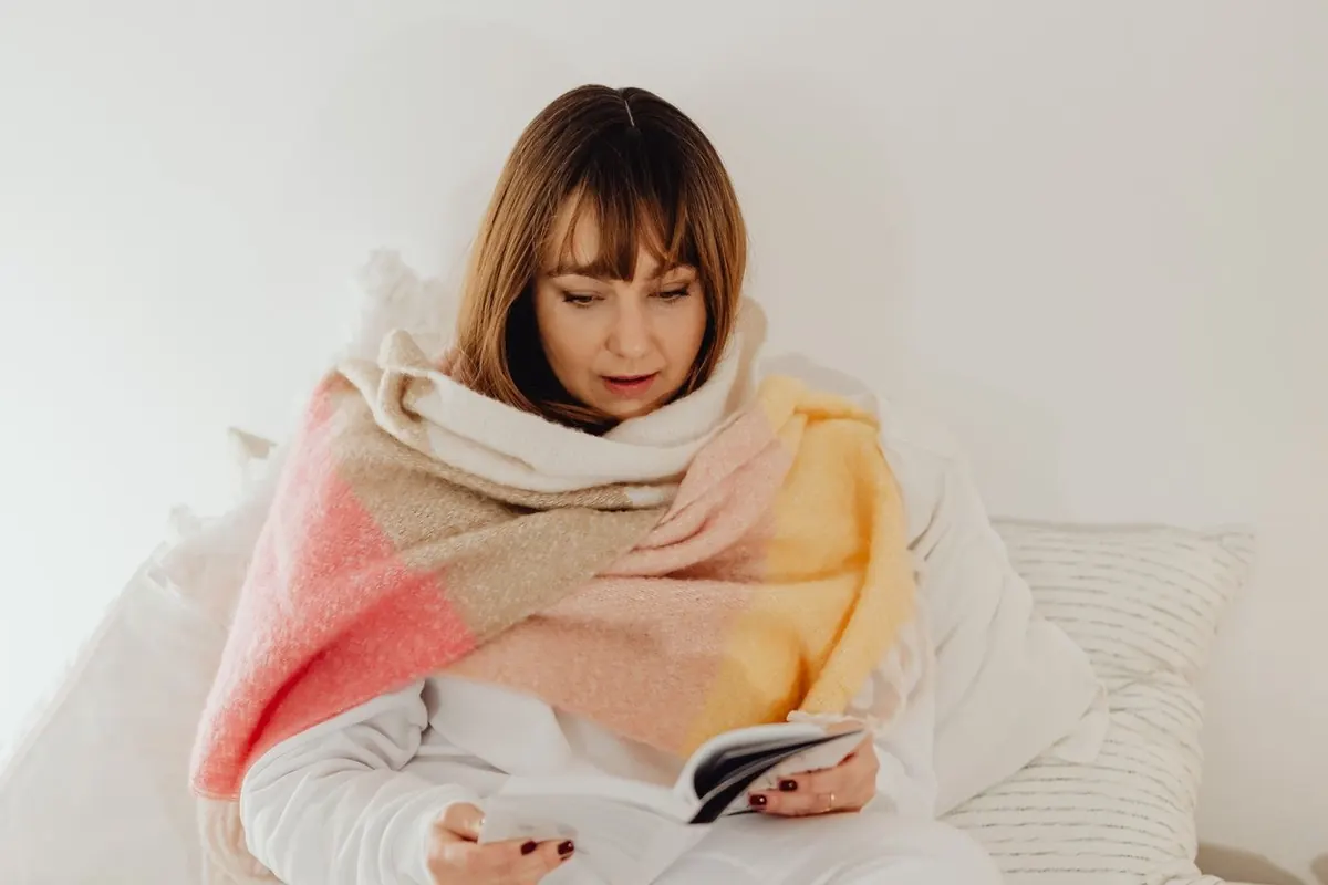 Femme qui lit, emmitouflée dans une couverture, avant de dormir