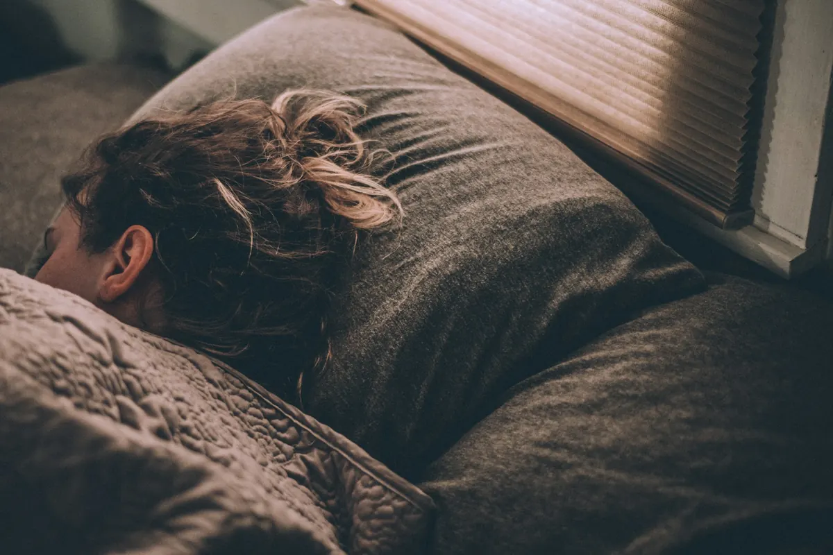 Personne endormie sous une couverture, le visage dans l'oreiller, dans une chambre à la lumière tamisée