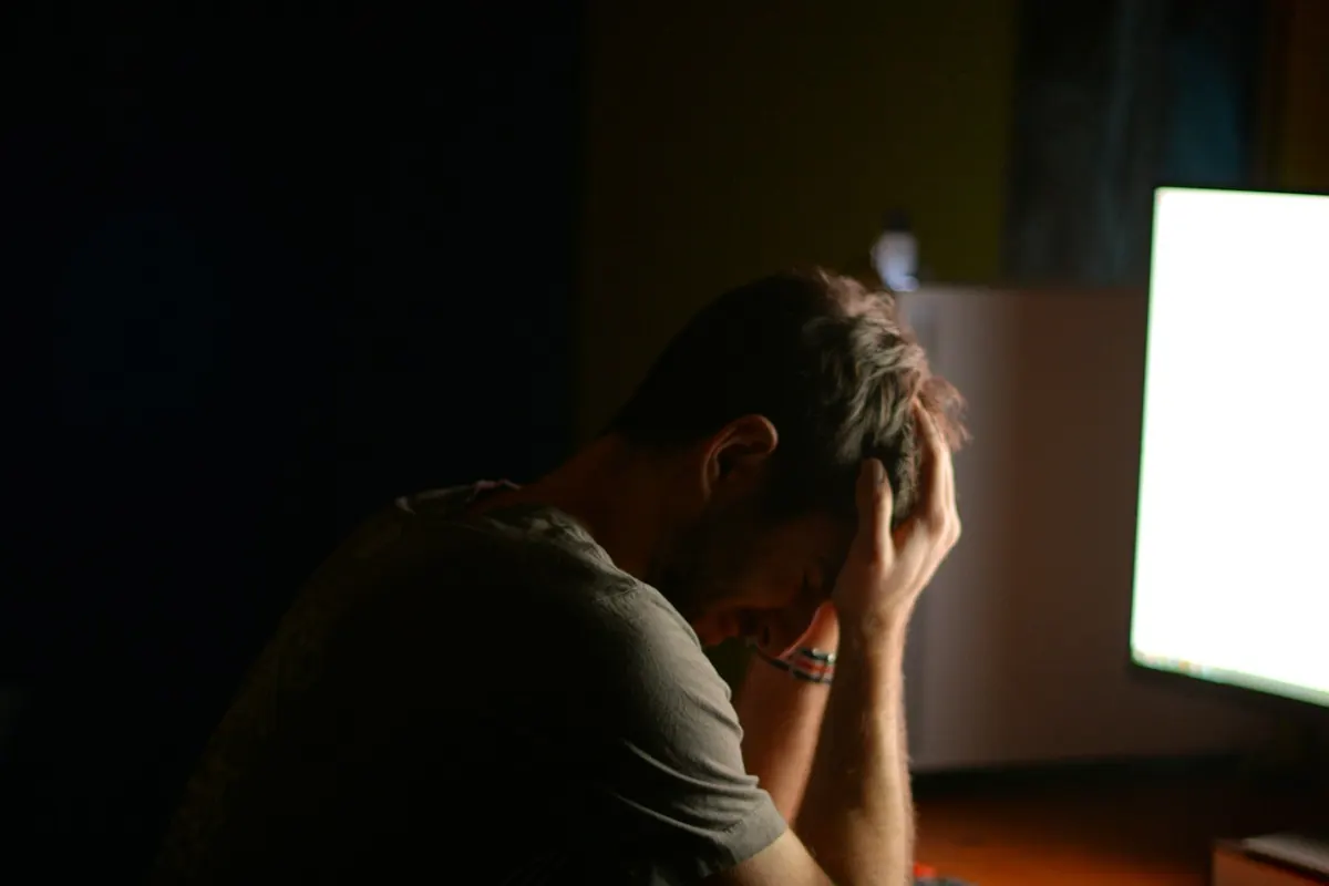 Homme épuisé à son bureau le soir, la tête dans les mains